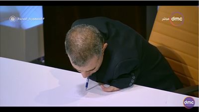 شاهد.. أول رئيس لإذاعة القرآن الكريم من ذوي الهمم يكتب بأسنانه على الهواء